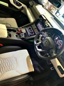 Interior view of a luxury car showcasing a leather-trimmed steering wheel, detailed dashboard with digital displays, center console with multiple controls and gear shifter, two-tone leather seats, and cup holders. The car has a sleek and modern design.